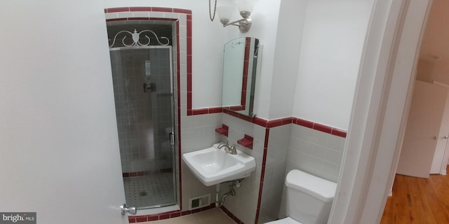 bathroom with toilet, sink, tile walls, a shower with door, and hardwood / wood-style floors