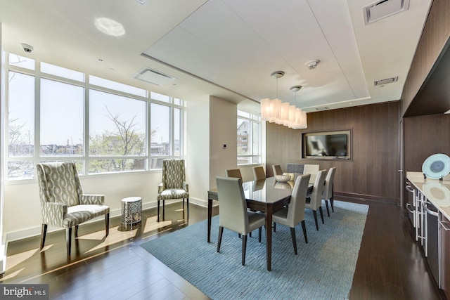 dining area with dark wood-type flooring, wood walls, and plenty of natural light