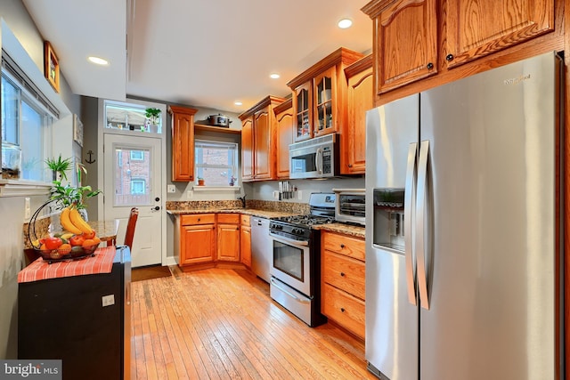 kitchen featuring appliances with stainless steel finishes, sink, light stone counters, and light hardwood / wood-style flooring