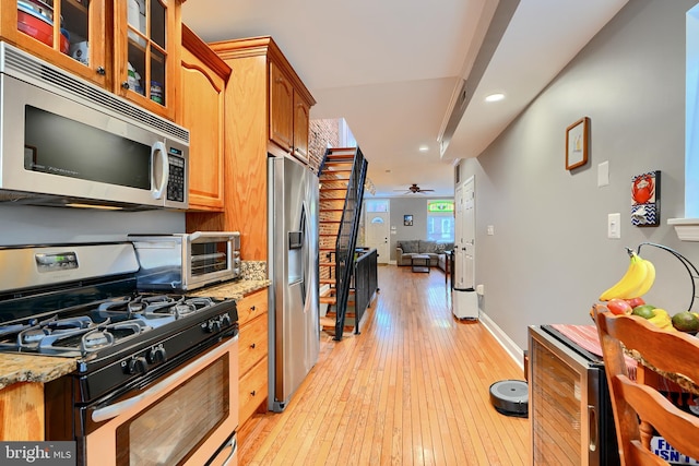 kitchen featuring wine cooler, light stone counters, light hardwood / wood-style flooring, ceiling fan, and stainless steel appliances