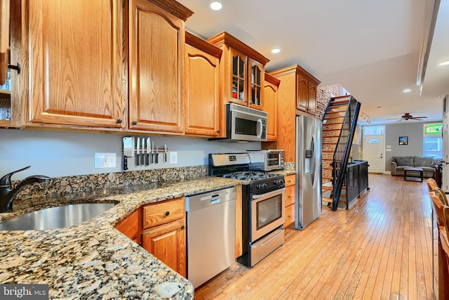 kitchen with sink, ceiling fan, stainless steel appliances, light stone counters, and light wood-type flooring