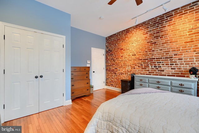 bedroom featuring rail lighting, ceiling fan, light hardwood / wood-style floors, brick wall, and a closet