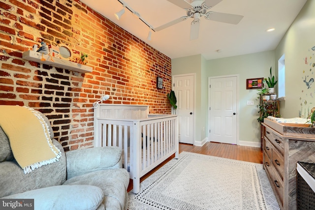 bedroom with ceiling fan, track lighting, light wood-type flooring, and a crib