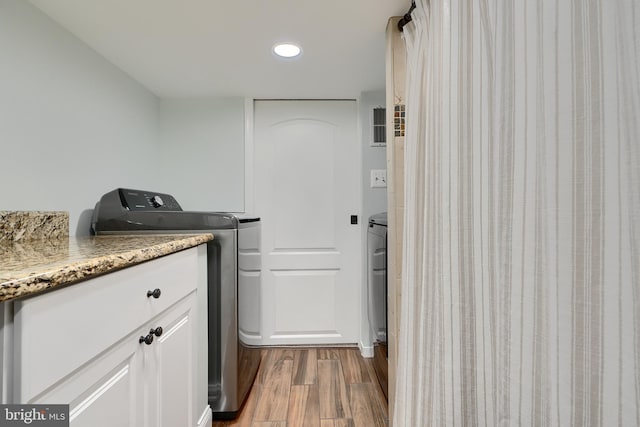 clothes washing area featuring cabinets, washing machine and clothes dryer, and dark hardwood / wood-style flooring