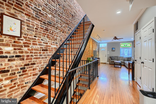 stairs with hardwood / wood-style floors, ornamental molding, ceiling fan, and brick wall