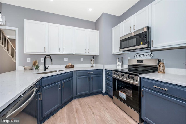 kitchen featuring sink, blue cabinetry, white cabinetry, stainless steel appliances, and light hardwood / wood-style floors