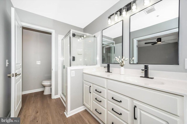 bathroom featuring a shower with shower door, wood-type flooring, vanity, ceiling fan, and toilet