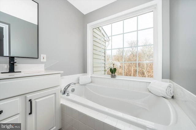 bathroom featuring a relaxing tiled tub and vanity