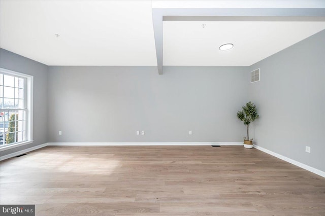 spare room featuring beamed ceiling and light hardwood / wood-style floors