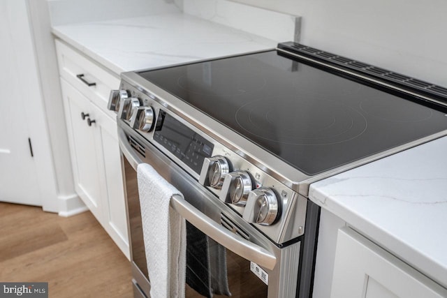 room details with stainless steel range with electric stovetop, light stone counters, white cabinetry, and light wood-type flooring