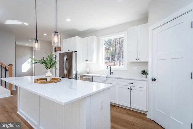 kitchen with stainless steel appliances, a center island, light stone countertops, white cabinets, and decorative light fixtures