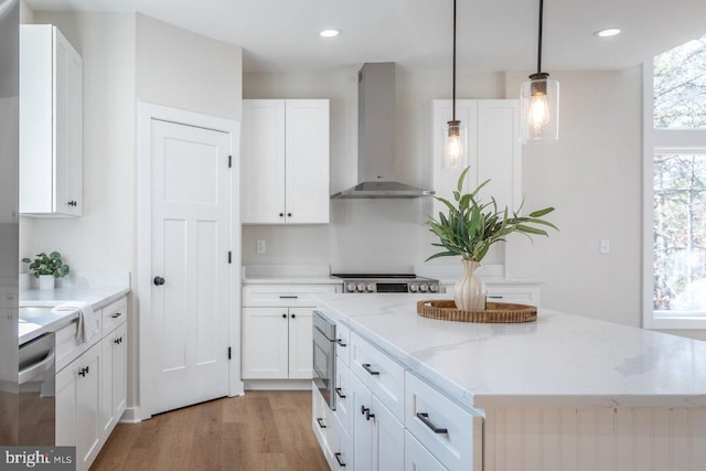 kitchen featuring white cabinetry, decorative light fixtures, a center island, light stone countertops, and wall chimney range hood