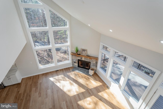 living room featuring a stone fireplace, high vaulted ceiling, and light wood-type flooring