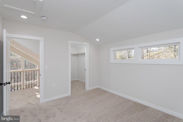 unfurnished bedroom featuring light colored carpet, vaulted ceiling, a closet, and a walk in closet