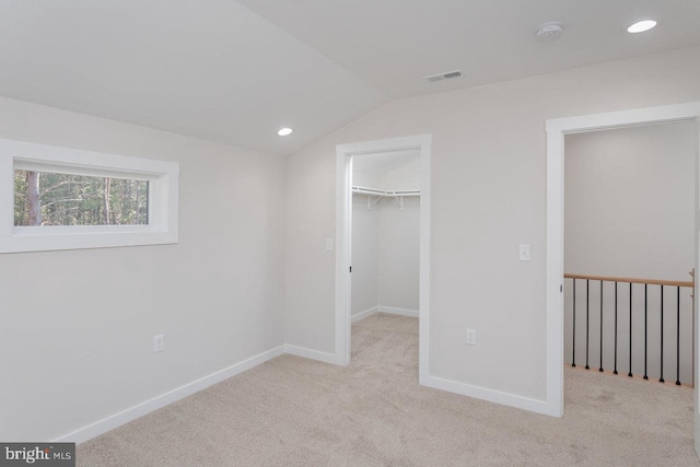 unfurnished bedroom with light carpet, a spacious closet, vaulted ceiling, and a closet