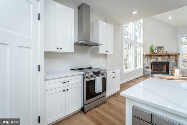 kitchen featuring electric stove, white cabinets, a fireplace, and wall chimney exhaust hood