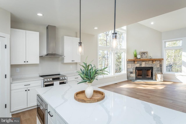 kitchen with light stone counters, decorative light fixtures, wall chimney range hood, stainless steel appliances, and white cabinets