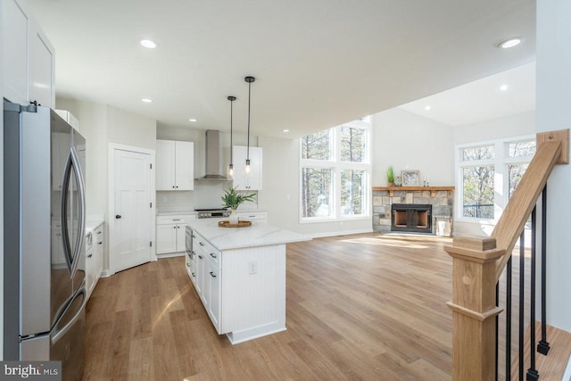 kitchen featuring wall chimney exhaust hood, decorative light fixtures, stainless steel fridge, a kitchen island, and white cabinets