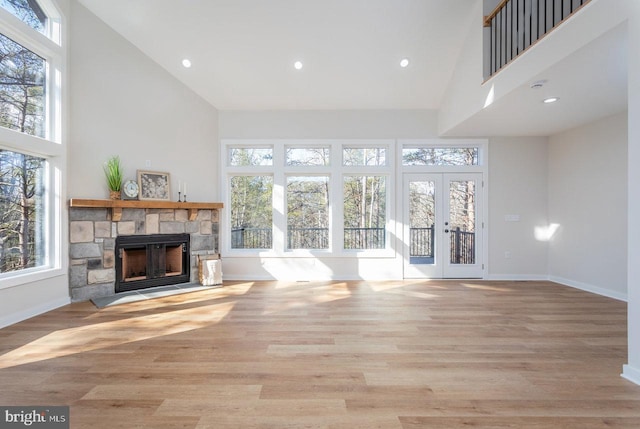 unfurnished living room featuring a healthy amount of sunlight, a fireplace, light hardwood / wood-style floors, and a high ceiling