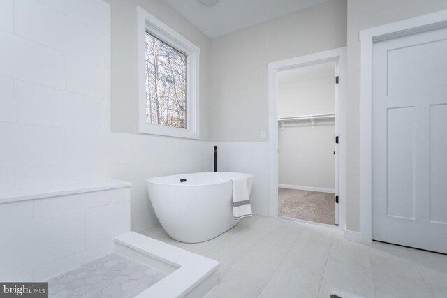 bathroom with tile walls, a tub to relax in, and tile patterned flooring