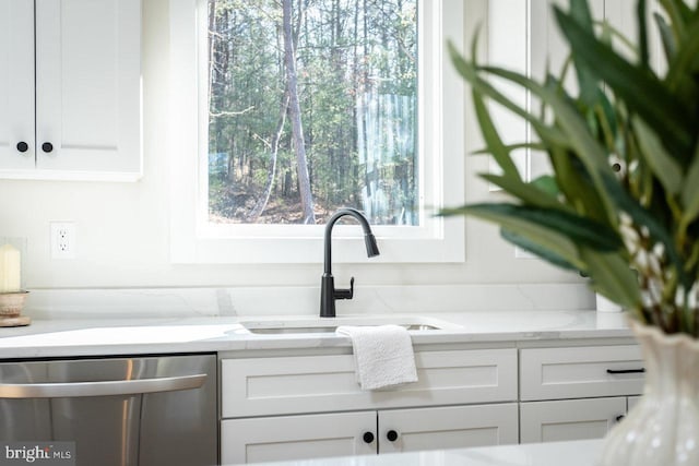 interior details featuring white cabinets, light stone countertops, sink, and dishwasher