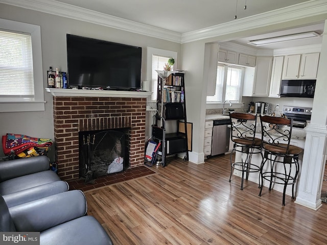 living room with sink, crown molding, wood-type flooring, and a brick fireplace