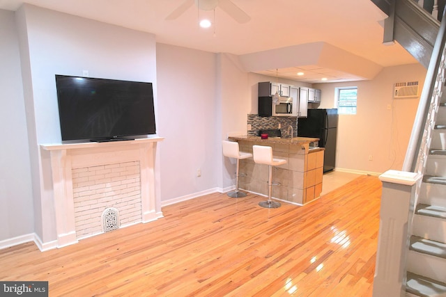 living room featuring a wall unit AC, ceiling fan, and light hardwood / wood-style flooring