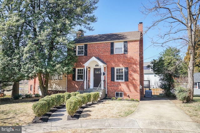 colonial house featuring brick siding, central air condition unit, and a chimney