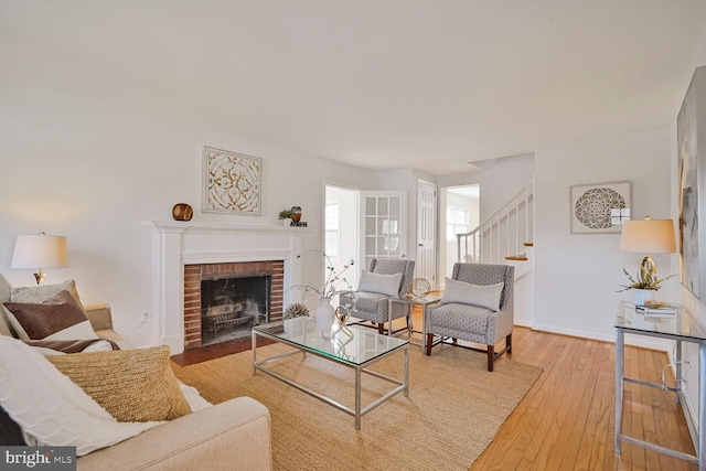 living area with stairway, baseboards, a brick fireplace, and hardwood / wood-style flooring