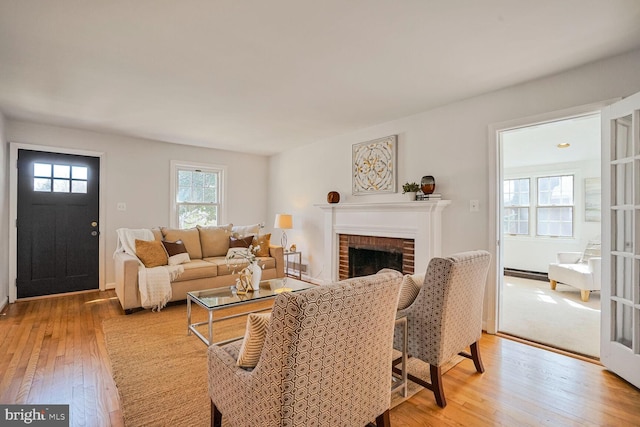 living area with a baseboard radiator, a brick fireplace, and light wood finished floors