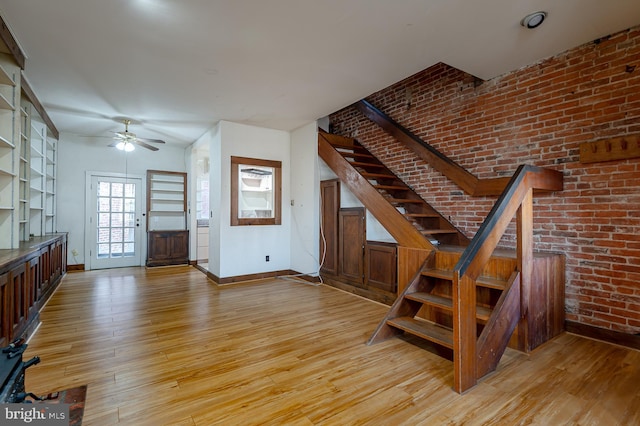 staircase with ceiling fan, brick wall, and wood-type flooring