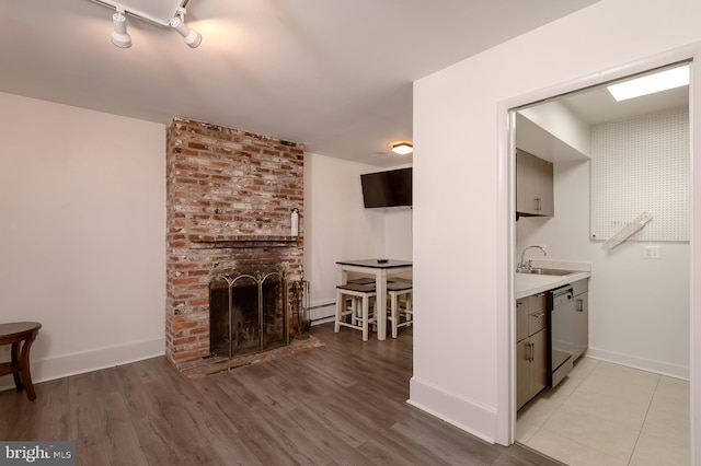 kitchen featuring sink, a brick fireplace, baseboard heating, dishwasher, and light hardwood / wood-style floors