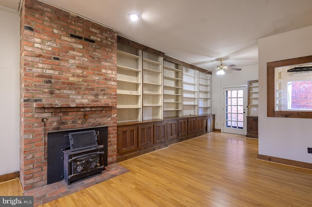 unfurnished living room with wood-type flooring, a wood stove, and ceiling fan