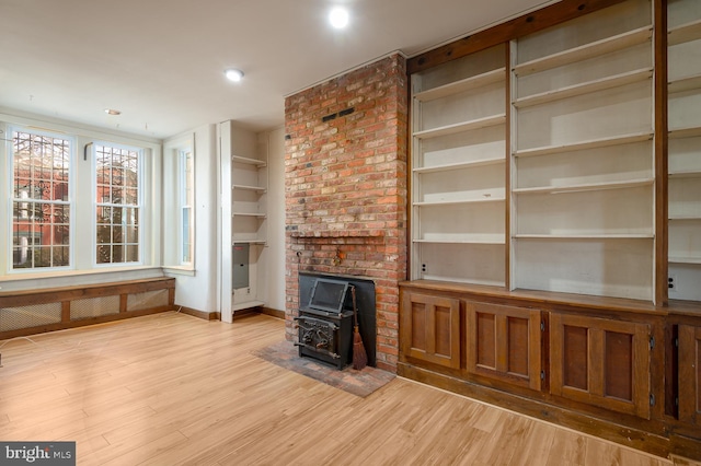 unfurnished living room featuring built in shelves, a wood stove, and light wood-type flooring