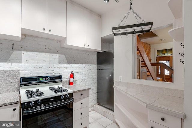 kitchen featuring gas stove, light tile patterned floors, black refrigerator, pendant lighting, and white cabinets