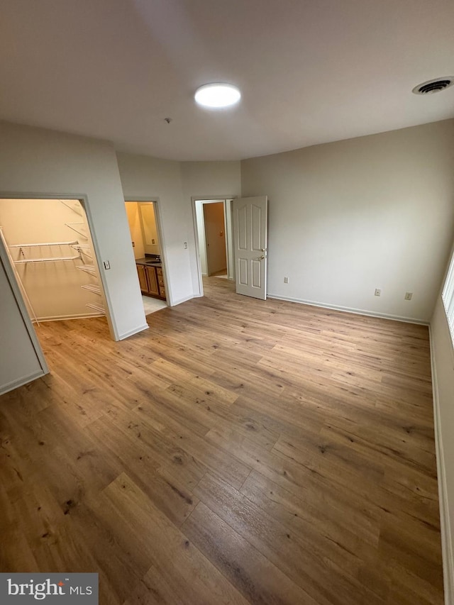 unfurnished bedroom with connected bathroom, a spacious closet, light hardwood / wood-style floors, and a closet