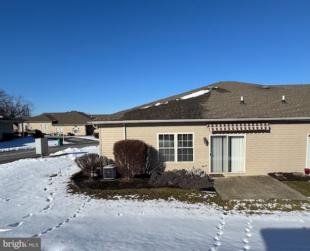 snow covered back of property featuring central AC unit