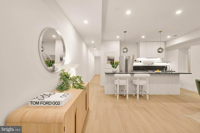 kitchen featuring stainless steel refrigerator, a breakfast bar, hanging light fixtures, white cabinets, and light wood-type flooring