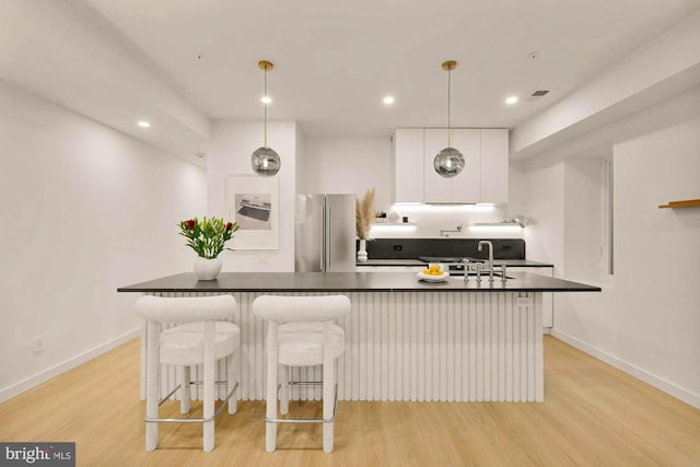 kitchen featuring white cabinetry, light hardwood / wood-style flooring, stainless steel refrigerator, a kitchen breakfast bar, and pendant lighting