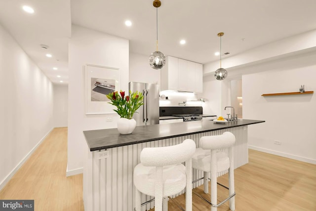 kitchen featuring a breakfast bar, high end fridge, decorative light fixtures, light hardwood / wood-style floors, and white cabinets