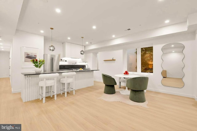 kitchen featuring a kitchen bar, white cabinetry, decorative light fixtures, light hardwood / wood-style flooring, and stainless steel fridge