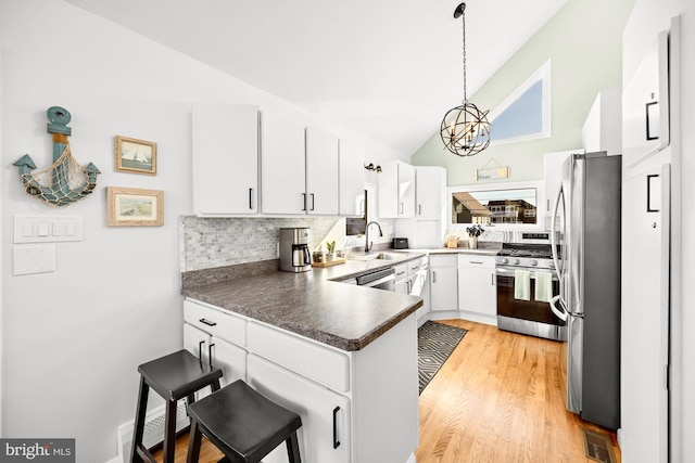 kitchen with hanging light fixtures, appliances with stainless steel finishes, a kitchen breakfast bar, kitchen peninsula, and white cabinets