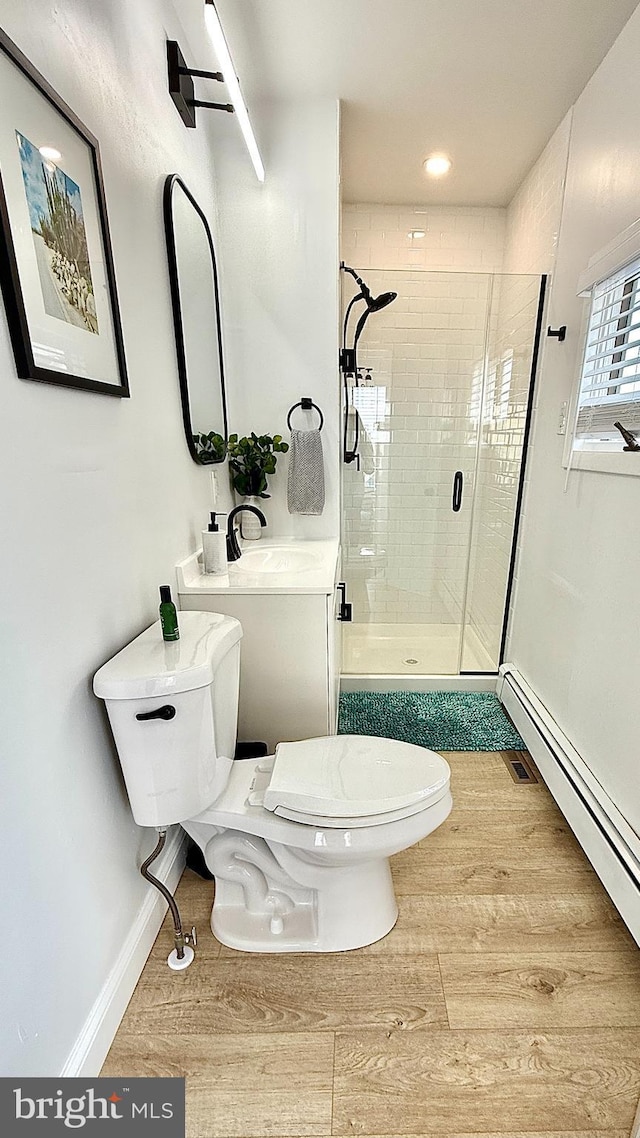 bathroom featuring hardwood / wood-style flooring, toilet, a baseboard heating unit, and walk in shower