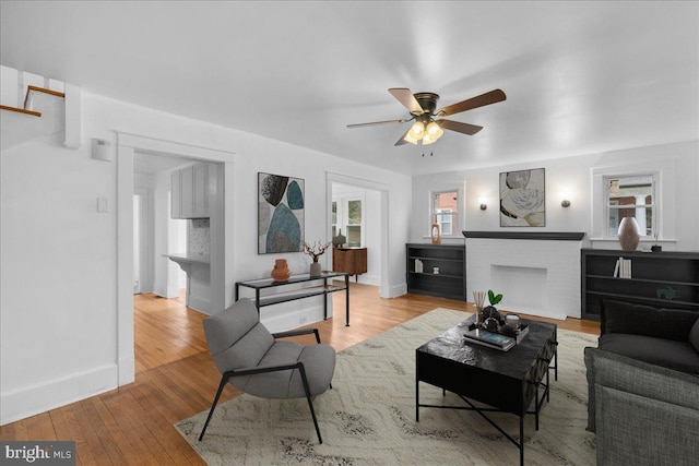 living room with ceiling fan, a fireplace, and light hardwood / wood-style flooring