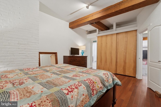 bedroom featuring beam ceiling, hardwood / wood-style flooring, a closet, and brick wall