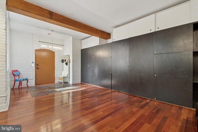 spare room featuring dark wood-type flooring, brick wall, and beam ceiling