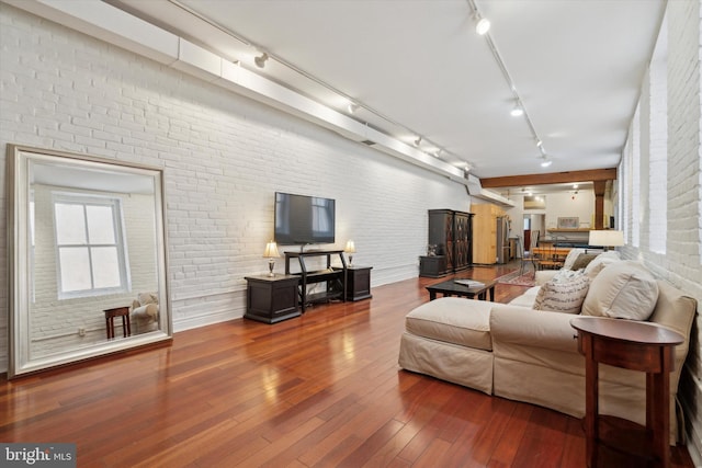 living room with hardwood / wood-style flooring, rail lighting, and brick wall