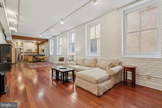 living room featuring dark wood-type flooring, rail lighting, and brick wall