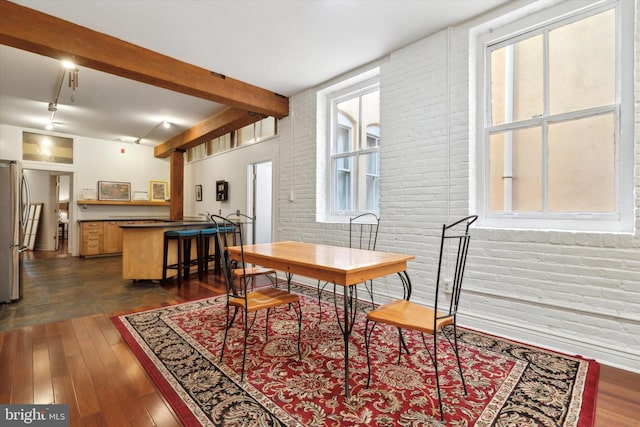 dining room with rail lighting, brick wall, dark hardwood / wood-style floors, and beam ceiling