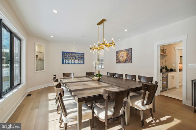 dining room with wine cooler, a healthy amount of sunlight, an inviting chandelier, and light hardwood / wood-style floors